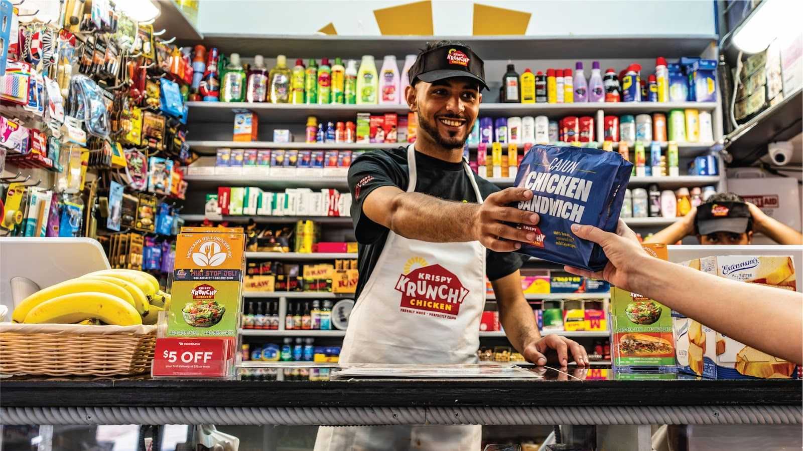 Store clerk handing a chicken sandwich to customer at a colorful convenience store counter.